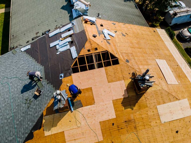 Person carefully replacing missing shingles on a residential pitched roof using hand tools.